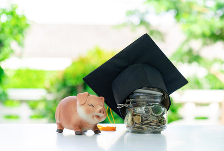 A piggy bank and a jar of coins covered with a cap, on a blurred background. Concept of saving and invesment about education.の写真素材