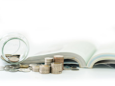 A jar of coins and an open book lie beside a pile of coins, representing the link between saving and learning isolate of white background.の写真素材