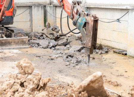 Close-up view of heavy machinery demolishing pavement with scattered debris and water.の写真素材