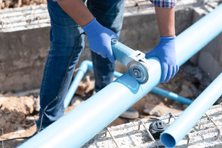 The worker is wearing blue protective gloves and jeans, ensuring safety while performing plumbing installation or repair.の写真素材