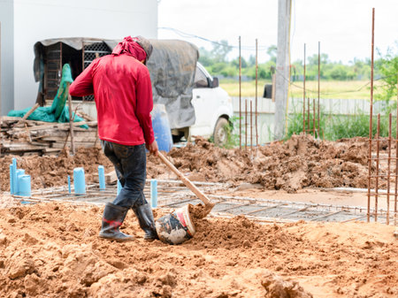 A bucket is used to move soil, while a white vehicle and construction materials are visible in the background.の写真素材