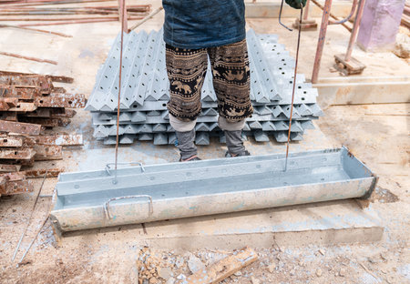 Close-up view of a construction worker dipping a steel component into a container filled with gray...