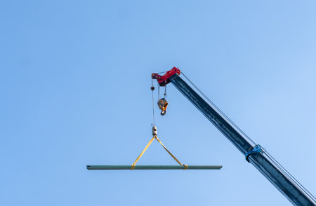 the boom and hook of a mobile construction crane against a completely clear, vibrant blue sky. The...