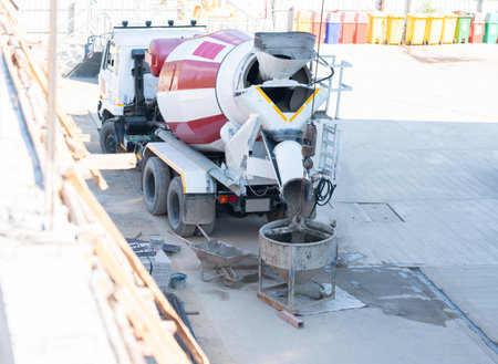 A construction series showing a cement mixer truck loading wet concrete into a crane bucket, which is then manually guided by workers to pour the foundation into formwork at a rural building site.の写真素材