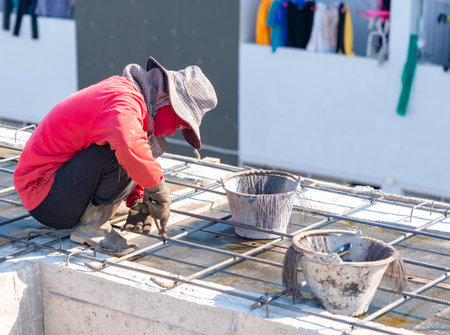 Construction worker in a red shirt tying steel reinforcement rebar with wire on a building site floor slab during daylight.の写真素材