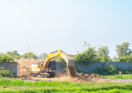 Heavy duty yellow crawler excavator working on a construction site, digging soil and moving earth against a clear sky background.の写真素材