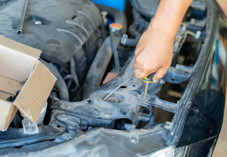 Close-up of a mechanic's hand using a screwdriver to tighten a bolt on a car engine, automotive repair and maintenance service in a professional garage.の写真素材