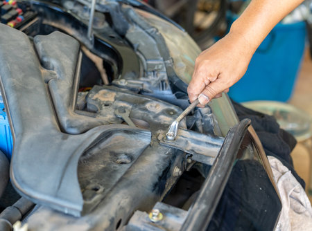 Professional mechanic repairing a car engine using a wrench to tighten bolts on the vehicle body frame in a workshop.の写真素材