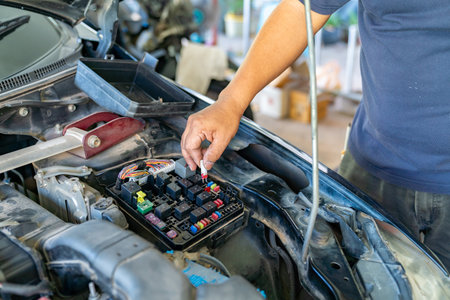 A high-angle, medium shot shows a mechanic's hand inserting a small red blade fuse into a car's fuse box located within the engine bay.の写真素材