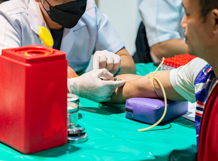 A features medical equipment including a yellow tourniquet, a purple armrest, a red biohazard sharps container, and multiple collection tubes in the background, set against a sterile green tabletop.の写真素材