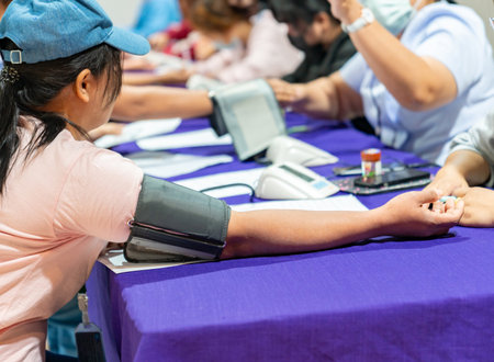 Close-up shot captures a row of people sitting at a long table covered with a purple cloth, undergoing blood pressure screenings at a community health event.の写真素材