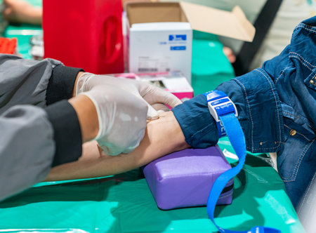 A high-angle, close-up shot showing a healthcare worker's gloved hands performing a venipuncture on a patient's arm.の写真素材
