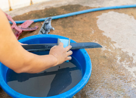 Close-up of a person hand wet sanding a black plastic car part with blue sandpaper in a water basin for surface preparation.の写真素材