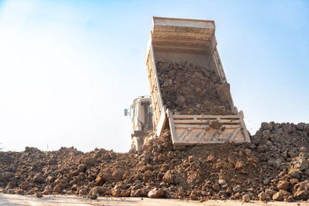 Large dump truck tipping and unloading a pile of soil and rocks at a construction or land...