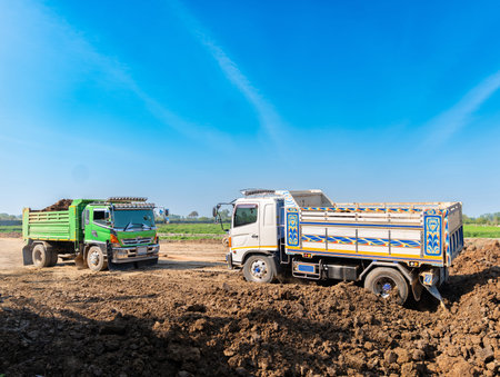 A green dump truck assisting and towing a white tipper truck stuck in deep mud at a construction site during land development.の写真素材