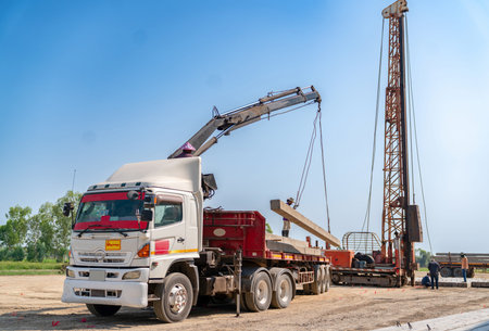 Heavy duty truck with crane unloading concrete piles for foundation work at a construction site.の写真素材