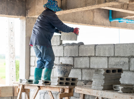 Construction worker building an interior concrete block wall from a wooden scaffold.の写真素材
