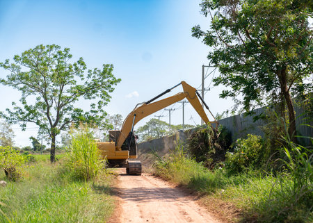 Heavy machinery in action: a construction excavator clearing brush and debris from the side of a country road, showcasing industrial land development in a rural landscape.の写真素材
