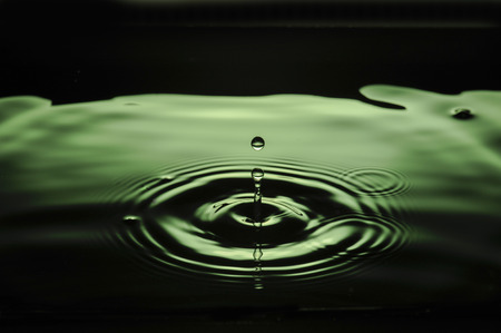 Double green waterdrop forming ripples in water and interesting suspended drop.  Commercial use.