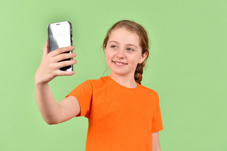 The girl in her hand has a mobile phone. A girl in an orange T-shirt. A baby on a green background.
