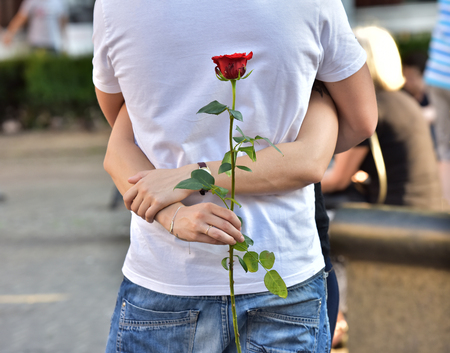 A girl hugs a guy with a flower in his hand. A rose in his hand.の写真素材