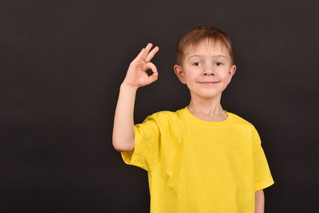 Cheerful boy on a black background. Happy childhood. A child in a yellow T-shirt. Children on a dark background.の写真素材