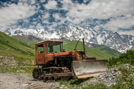 Old rusty corroded belt bulldozer parking in mountain landscape under the highest Georgian mountain Shkhara. Caucasus, Svaneti region, Georgiaの写真素材