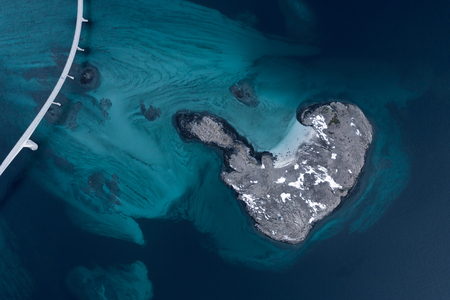Aerial shot of an island and bridge over sea strait. Visible depth with blue and green colours and snow near Tromso. Sommaroy, Norwayの写真素材