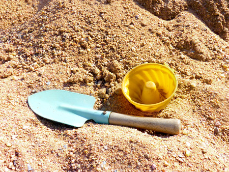 Close up of toy shovel and plastic cake on the sandbox sand.の写真素材