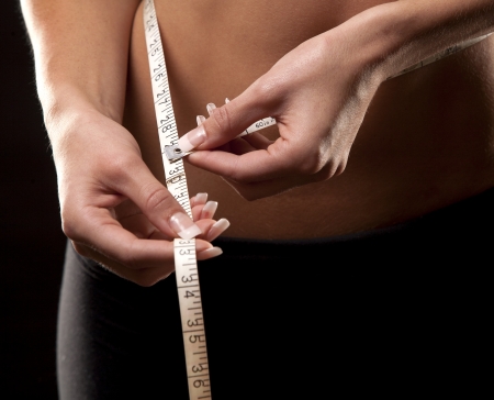fitness model is measuring her waist on black backgroundの写真素材