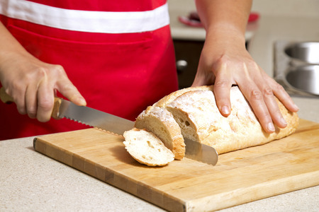 caucasian woman cutting a bread with knife in kitchen