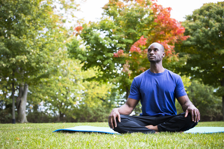 young black man wearing athletic wear sitting in the park exercising yogaの写真素材