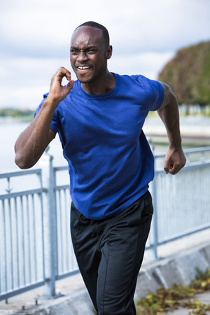 young black man wearing athletic wear running around the lakeの写真素材