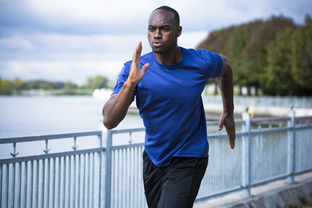 young black man wearing athletic wear running around the lakeの写真素材