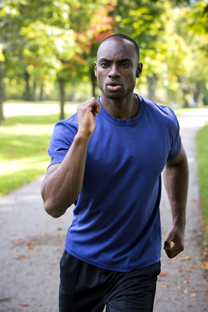 young black man wearing athletic wear running in the parkの写真素材