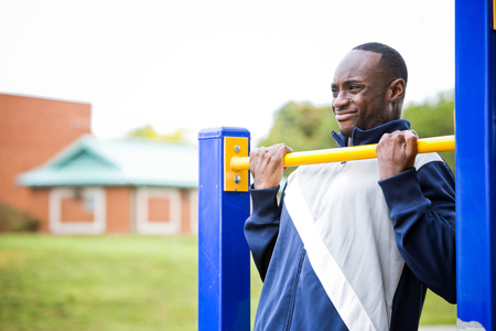 Active black man in training suit exercising at outdoor gym