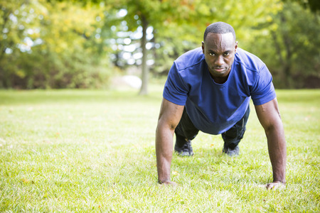 young black man wearing athletic wear doing exercise in the fall parkの写真素材