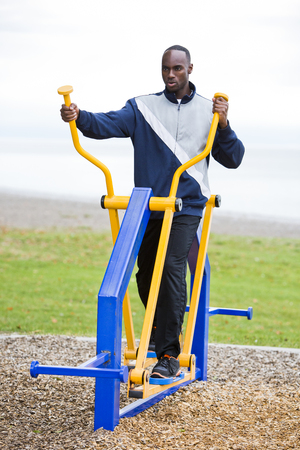 Active black man in training suit exercising on elliptical trainer machine at outdoor gymの写真素材