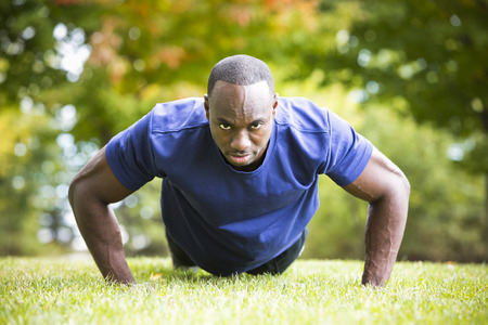 young black man wearing athletic wear doing exercise in the fall parkの写真素材