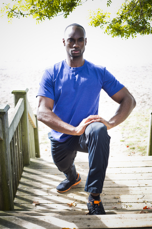 young black man wearing athletic wear sitting on the beach exercising yogaの写真素材