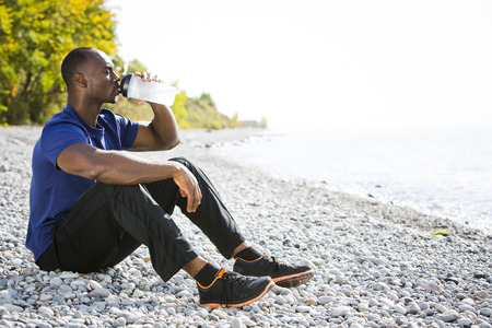 young black man wearing athletic wear sitting on the beachの写真素材