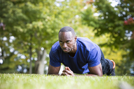 young black man wearing athletic wear doing exercise in the fall parkの写真素材