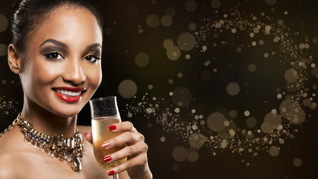 romantic Indian woman with golden makeup and nailpolish. Big gold fashion necklace. Black isolated background. Holding glass of champagne.の写真素材
