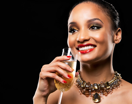 romantic Indian woman with golden makeup and nailpolish. Big gold fashion necklace. Black isolated background. Holding glass of champagne.の写真素材