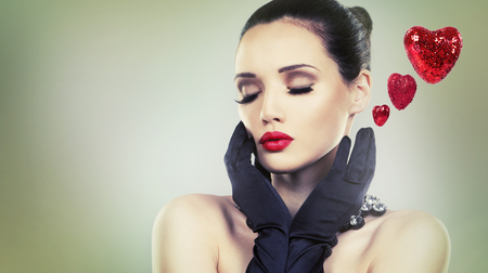 Upscale woman wearing jewellery and red lipstick on light background. Love hearts for Valentines Day.の写真素材