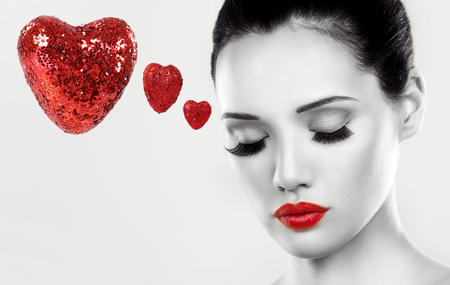 beautiful woman with dark makeup and red lipstick posing on light grey background. Black and white image. Red Valentines hearts.の写真素材