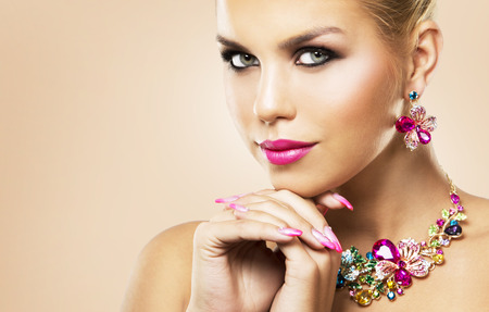 beautiful woman with dark makeup and pink lipstick posing on light beige background wearing flower spring and summer jewellry necklaceの写真素材