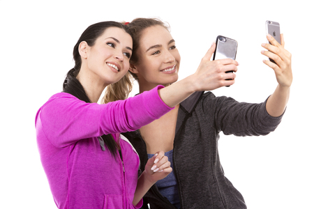 young casual caucasian women wearing sport outfits on white isolated background. Holding mobile phones.の写真素材