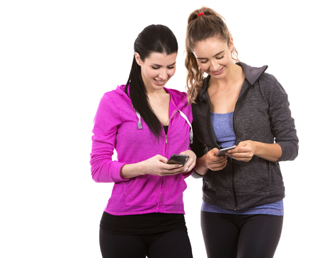 young casual caucasian women wearing sport outfits on white isolated background. Holding mobile phones.の写真素材