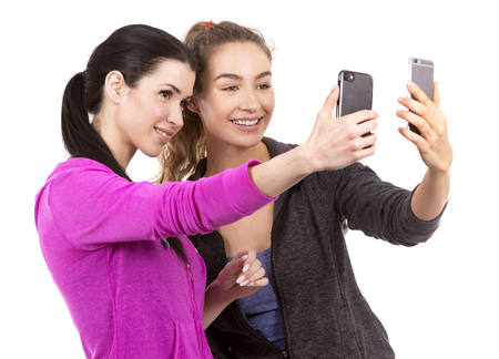 young casual caucasian women wearing sport outfits on white isolated background. Holding mobile phones.の写真素材